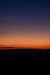 Vertical shot of a natural landscape with the city in the distance, glowing in the sunset. 