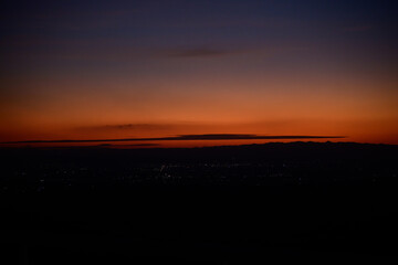 Wide shot of a natural landscape with the city in the distance, glowing in the sunset.