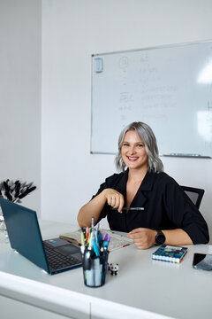 Portrait of a young beautiful English teacher working at school, at her desk in the classroom.