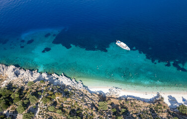 Drone Aerial view of tourists enjoying summer on a Greek isolated tropical beach with turquoise water.