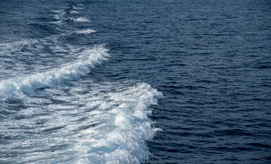 Boat wake creating white foaming waves on deep blue ocean water