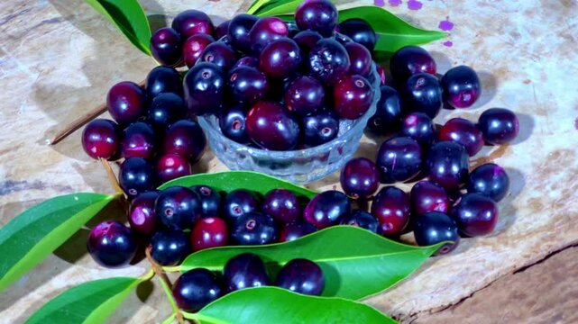 A bowl of java plums surrounded by java plum leafs on a rotating table