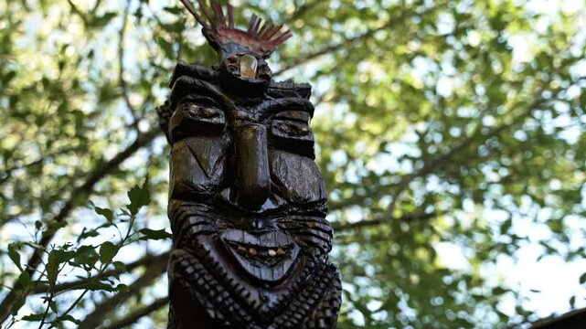 A large cultural statue of a Tiki God with a large leafy green tree in the background