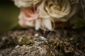 Elegant wedding rings on a textured stone surface with a romantic floral backdrop