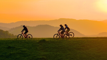 AERIAL, SILHOUETTE, LENS FLARE: Cyclists riding along a scenic hilltop at sunset. Vibrant glowing...