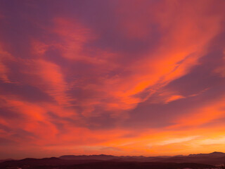 Expansive sky with a palette of orange and pink hues as sun sets behind distant mountain horizon. Tranquil beauty of nature at twilight, with vibrant sky contrasting against darkening land below.