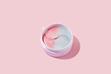 Hydrogel colorful patches for moisturizing and nourishing the skin around the eyes. Cosmetic product in a jar on a pink background. Minimal cosmetic product concept