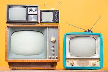 Retro TVs on table front yellow background. Vintage old style filtered photo