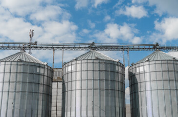 Tall metal silos are positioned against a backdrop of fluffy clouds, showcasing a modern agricultural setting that highlights food storage and production