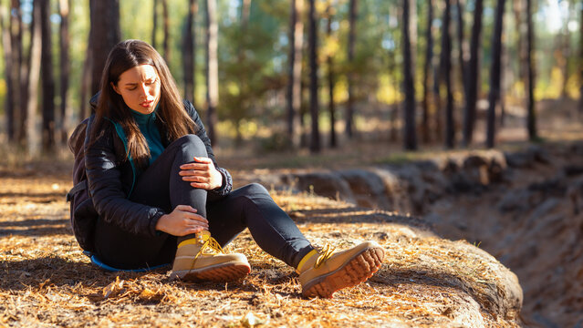 Crying girl rubbing her ancle and sitting on the ground in forest, woman injured her leg while hiking, empty space