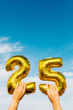 Hands holding number 25 golden balloons against blue sky