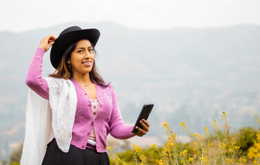 Foto de una feliz y bonita campesina con un sombrero hablando por un teléfono celular en los Andes peruanos. Mujer usando teléfono móvil