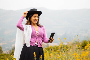 Foto de una feliz y bonita campesina con un sombrero hablando por un teléfono celular en los Andes...