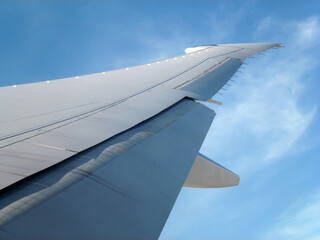 A perspective view of the wing of a flying passenger plane against a blue sky