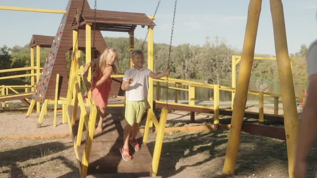 A father pushes his two young children on a swing set at the park. They are all smiles and laughter as they enjoy the beautiful summer day.