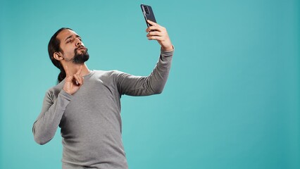 Man using smartphone to take selfies and post them on social media, studio backdrop. Vain person...