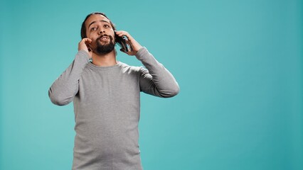 Joyous man catching up with friends in phone call using cellphone, studio background. Portrait of radiant person having conversation with mates during telephone call, camera B
