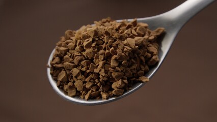 Spoonful of Instant Coffee Granules on brown background. Close-up, shallow dof.