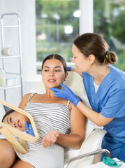 Woman cosmetologist examines patients face after lifting procedure and gently palpates touches chin...