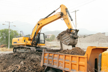 Excavator digging in the ground and loading soil into dump truck