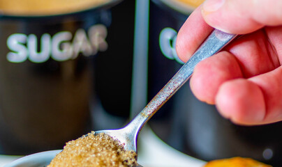 A teaspoon full of demerara sugar,being put into into a small,white cup of hot espresso coffee,in a domestic kitchen,Worcestershire,United Kingdom.