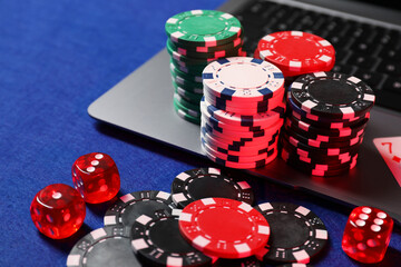 Poker chips, laptop and dices on blue table. Online game