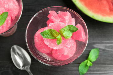 Tasty watermelon sorbet with mint in glass dessert bowl and spoon on black table, flat lay
