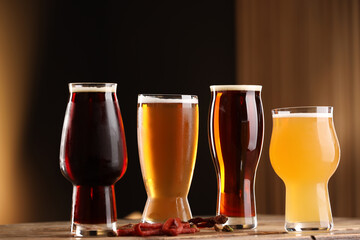 Glasses with different types of beer and snacks on wooden table against color background