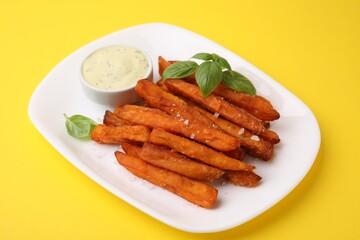Sweet potato fries, basil and sauce on yellow background, closeup