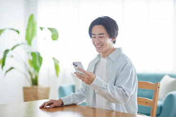 リビングでスマートフォンを使用する日本人大学生の男性