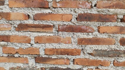 A close-up of a brick wall, showcasing the rustic texture of red brick with a layer of grey mortar in between.
