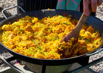 Close up while cooking a paella with vegetables, pork and seafood outdoors