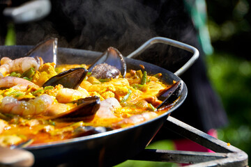 Close up while cooking a paella with vegetables, pork and seafood outdoors
