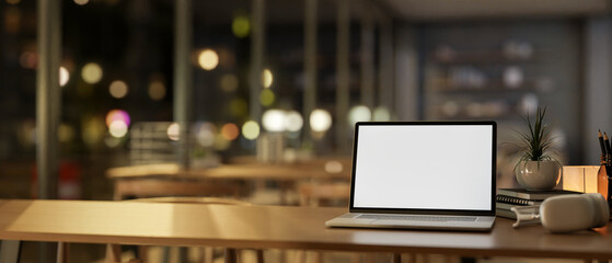 A laptop on a wooden table in a cozy contemporary restaurant or a coffee shop at night.