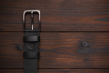Black Leather Belt with Metal Buckle on Rustic Wooden Background