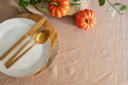 Minimalist Thanksgiving table setting, rustic plate napkin, gold cutlery and autumn pumpkin decoration on linen blackguard, copy space
