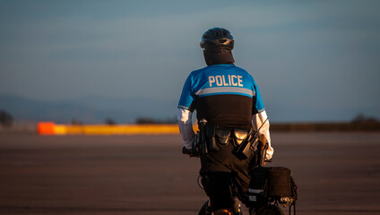A police officer on a bicycle patroling a large asphalt area in later afternoon sunlight . The...
