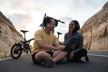 male and female hijab biker using tablet and laughing together