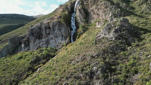 Aerial ascends mountain slope to Caryacuyo Waterfall in southern Peru