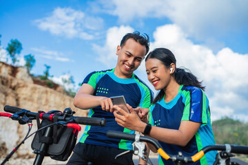 female and male biker using phone when riding bicycle, with pointing gesture