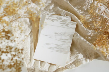 Card blank mockup empty paper, envelope and dry flowers on beige fabric linen texture background top view flat lay. Copy space. Greeting card mock up.