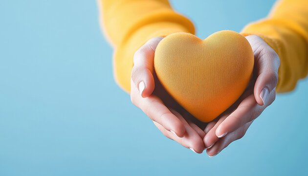 A person holds a soft yellow heart, symbolizing love and care, against a calm blue background, conveying warmth and affection.