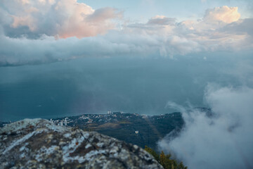 Majestic panoramic view of ocean and clouds from mountain top with person sitting on rock, contemplating nature and travel experience