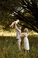 Naklejka premium A family of three, a man and a woman with a child in their arms, stand in a park in the summer. The concept of a happy family with a small child, care and love.