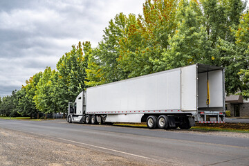 Long hauler white big rig semi truck with dry van semi trailer with open back door standing on the street shoulder ready to go to dock gate for load next cargo © vit