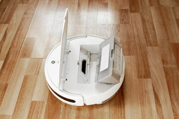 Container filled with trash and dust after cleaning next to robot vacuum cleaner with an open lid