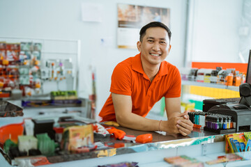 handsome male shopkeeper smiles at the camera while leaning on the minimarket cash register