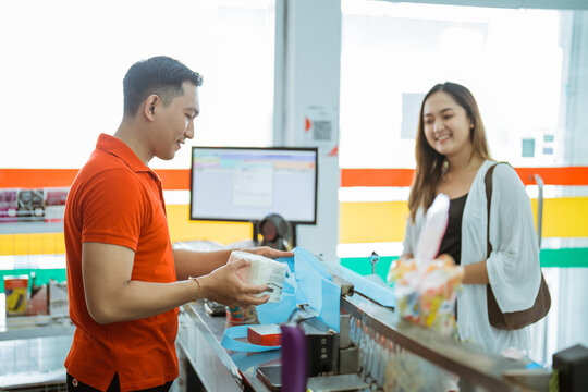 male shopkeeper putting shopping items into plastic bag while serving female shoppers in minimart