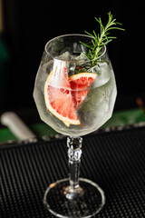 Refreshing gin and tonic cocktail with grapefruit and rosemary in a beautiful bar.
