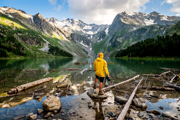 a man stands on the shore of a mountain lake with a camera